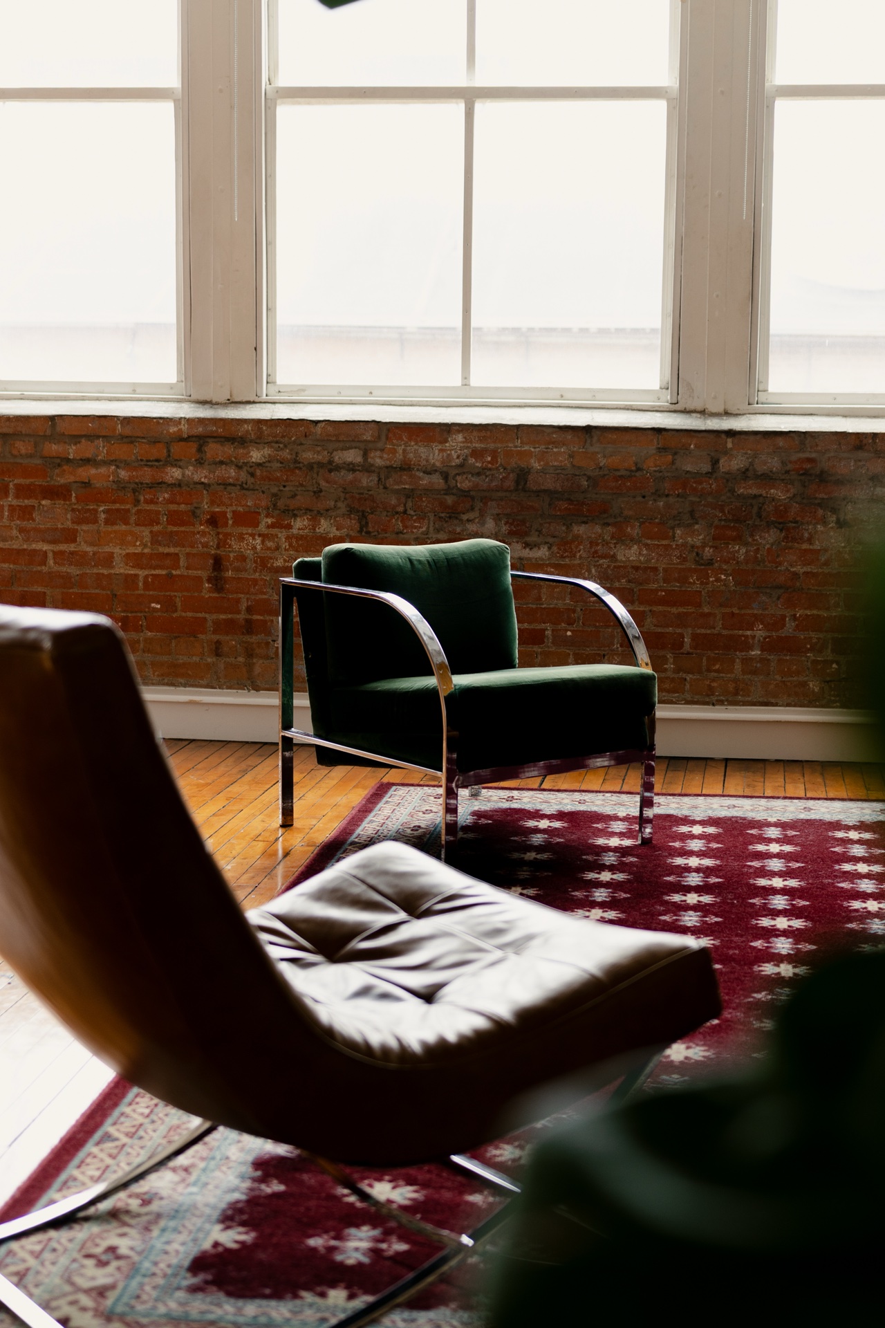A green armchair and a leather lounge chair on a red patterned rug